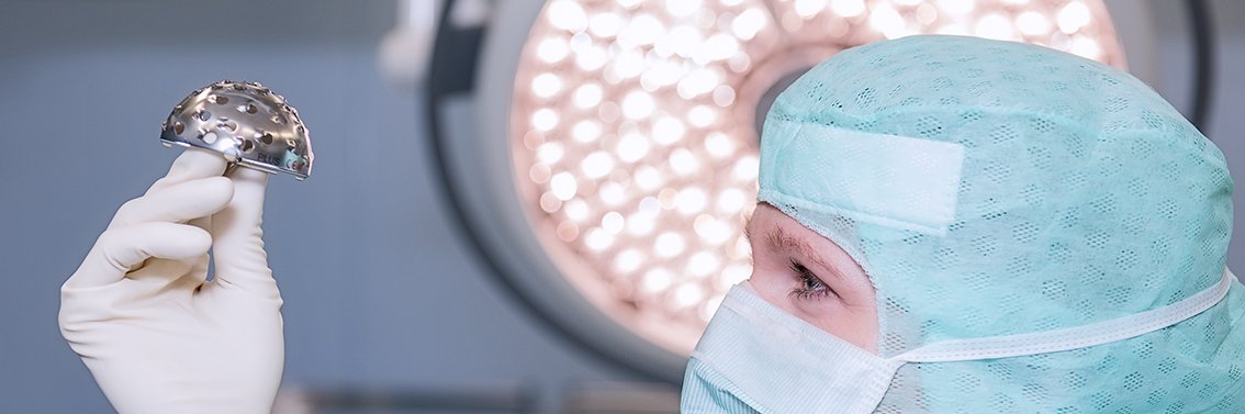 Frau in OP-Kleidung hält ein medizinisches Gerät in den Händen und schaut es sich genau an