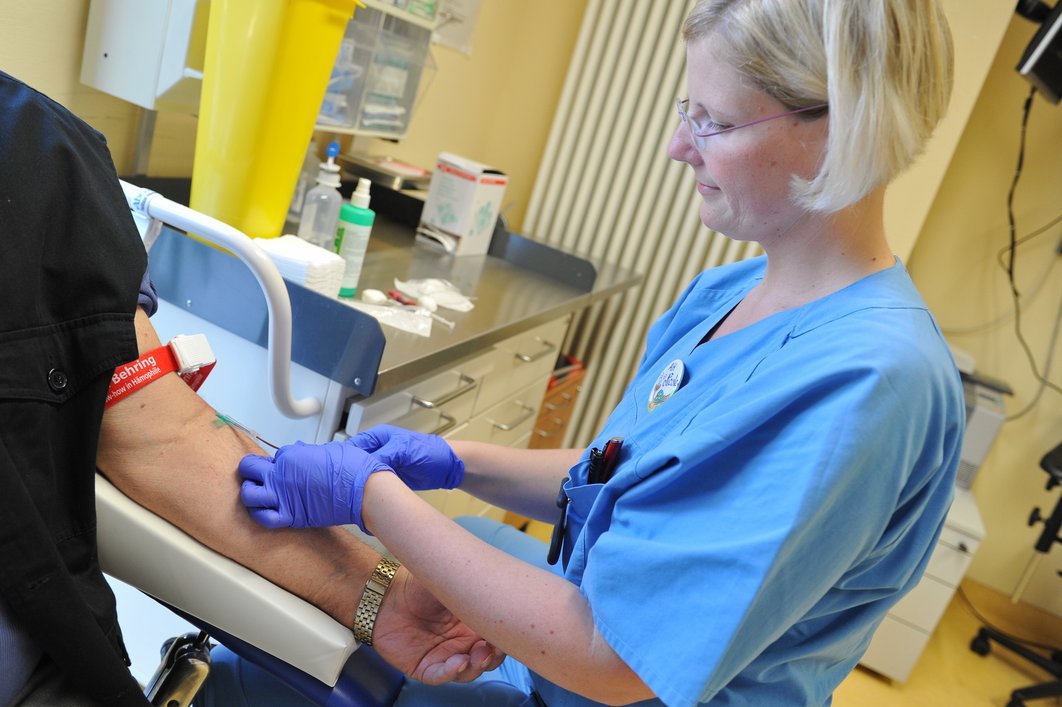 Frau im blauen Kittel nimmt einem Patienten Blut ab