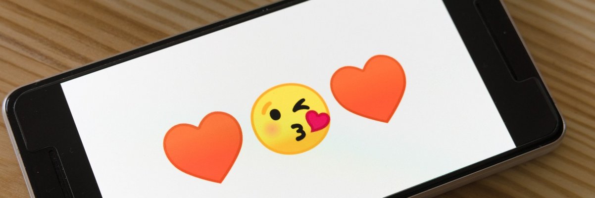Ein Smartphone, auf dem drei große Emojis nebeneinander zu sehen sind: Herz, Kuss-Gesicht, Herz